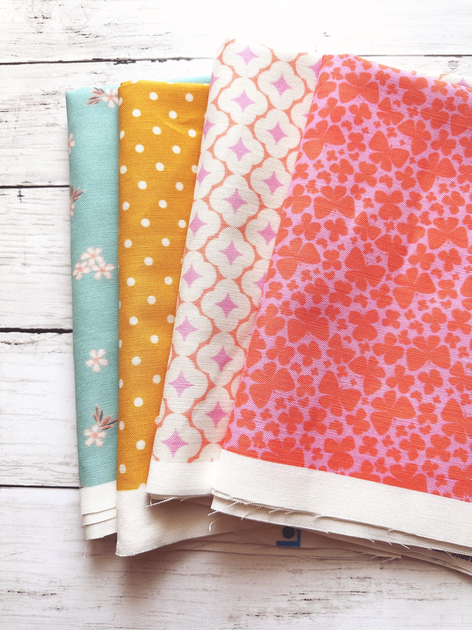 Four fabrics fanned out on a white surface. Bright pink with butterflies. White with peach rounded diamonds. Yellow and white polka dots. And blue with tiny white flowers.