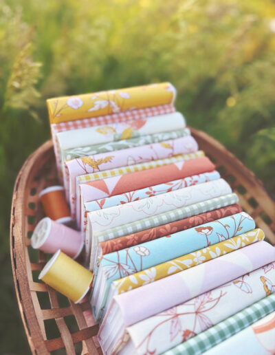 Buttercup Hill fabric collection from Sincerely Yours Kimberly. The fabrics are shown in a wildflower field at the golden hour in a wooden basket. The collection is about vintage farmhouse. Summer evenings in grandma's kitchen. The fabrics are available at Spoonflower.